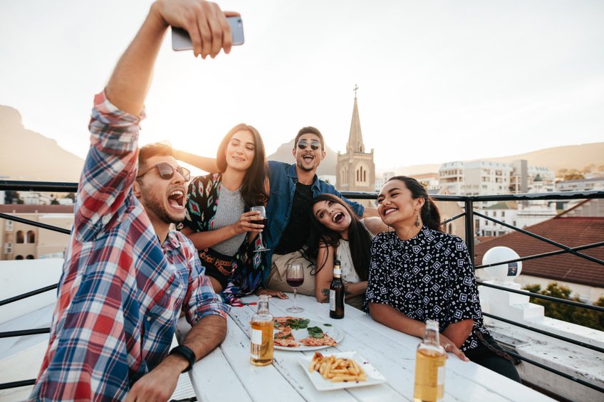 Grupo de amigos composto de dois homens e três mulheres tirando uma selfie em um restaurante