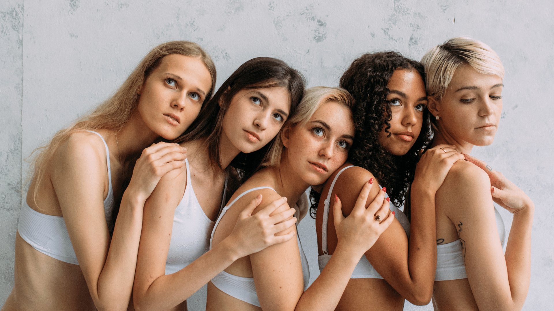 Grupo de cinco mulheres de diversas etnias abraçadas com uma expressão séria