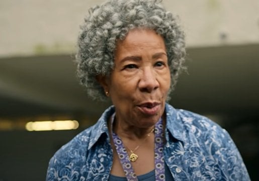 Personagem Denise da série Maid com uma busa azul, cabelos grisalhos e cacheados