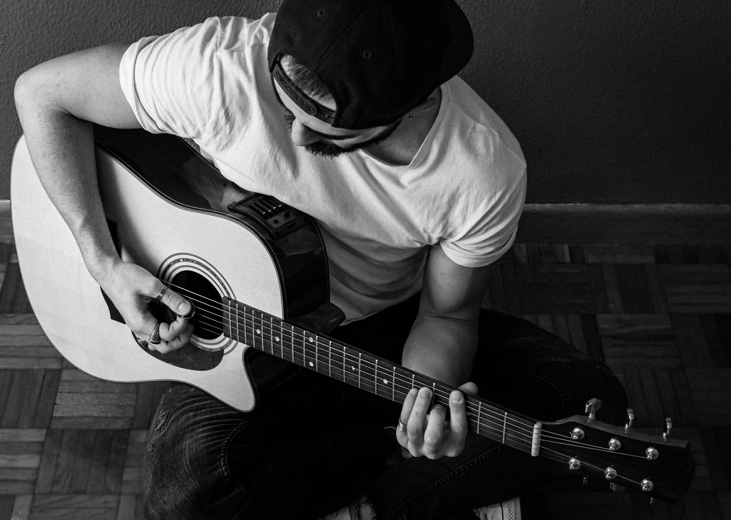 Homem de boné tocando violão. Imagem preta e branca