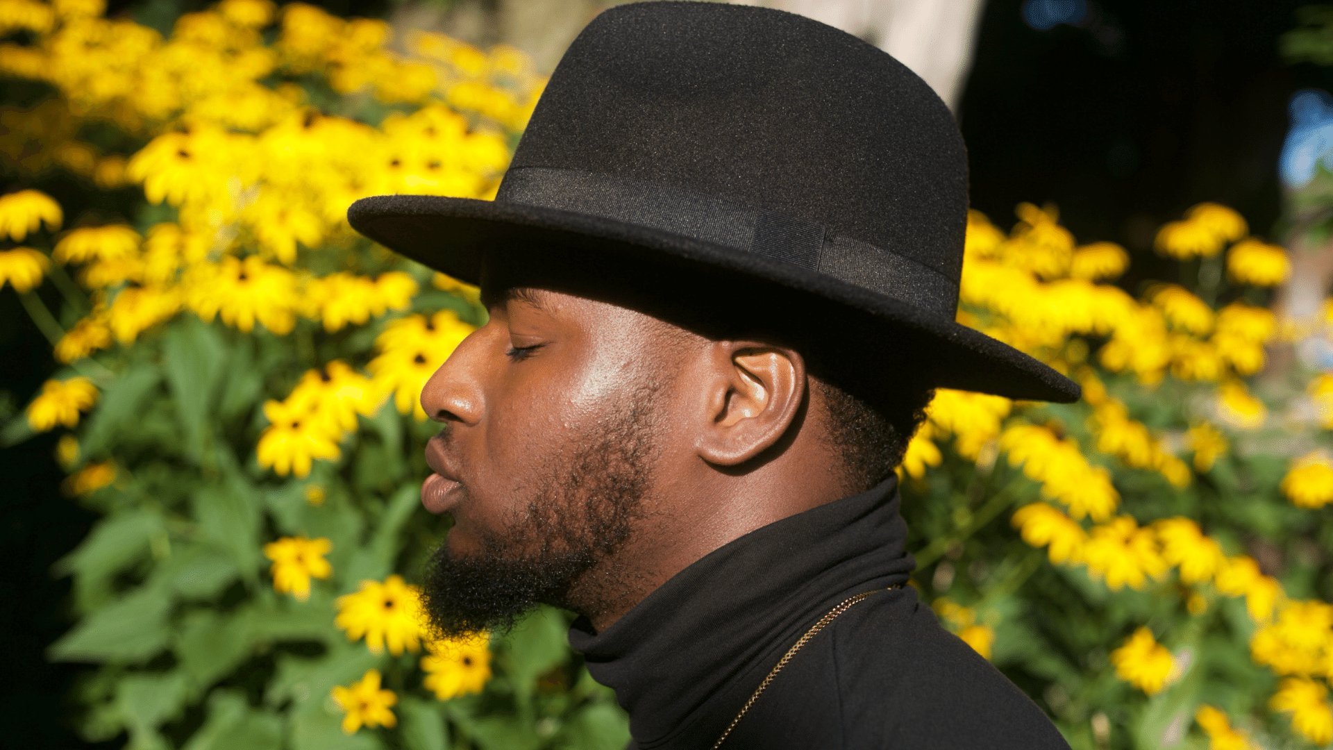 Homem negro com o rosto voltado para frente de olhos fechados usando um chapéu