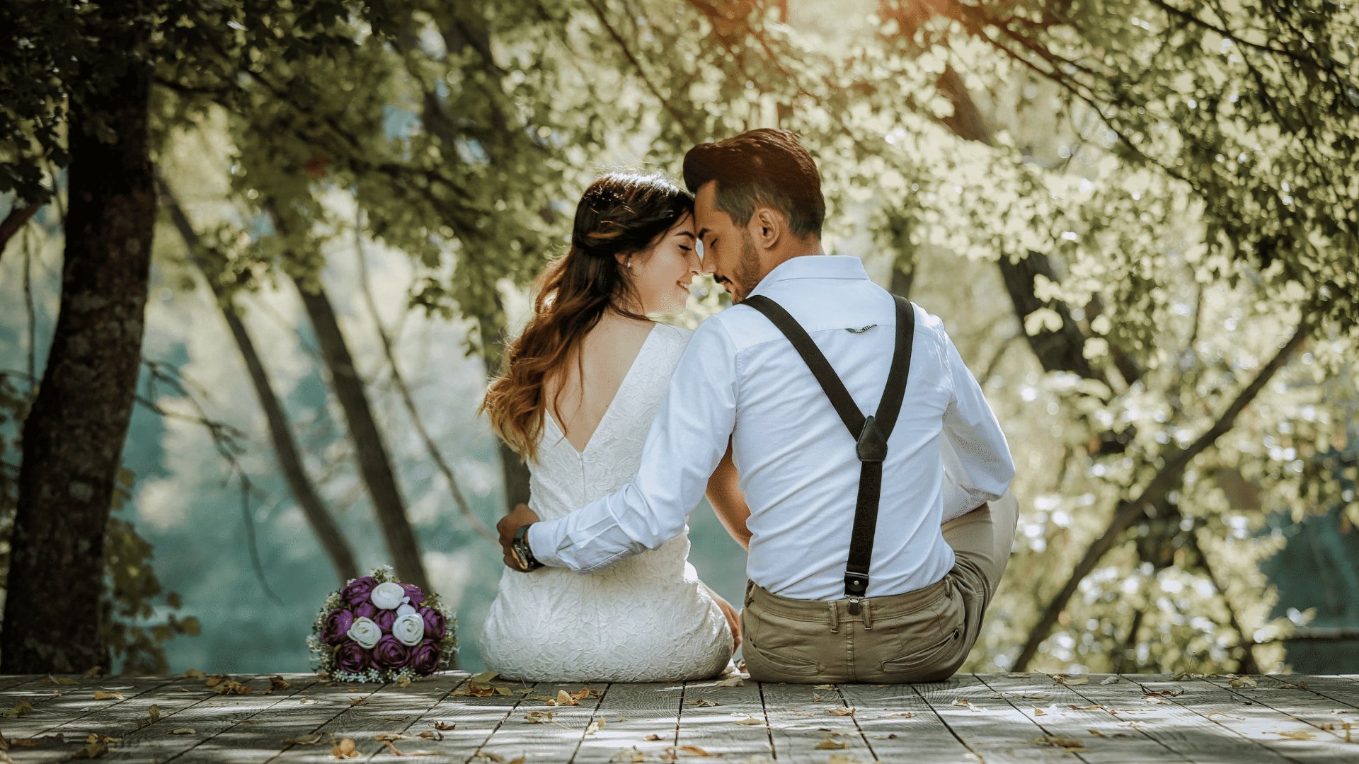 Casal abraçado sentado em um estrado de madeira em meio a natureza