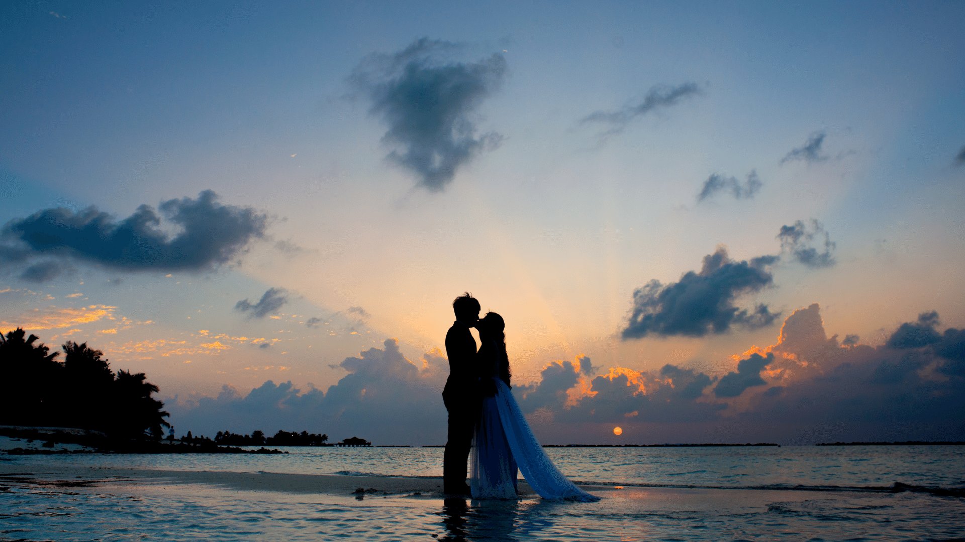 Casal se beijando na beira do mar enquanto o sol está se pondo