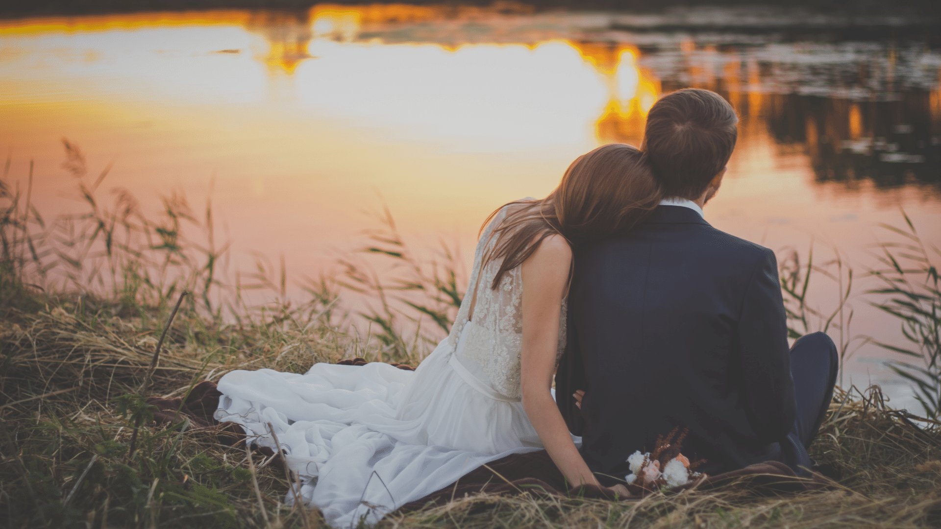 Casal sentado de costas na grama em frente a um lago