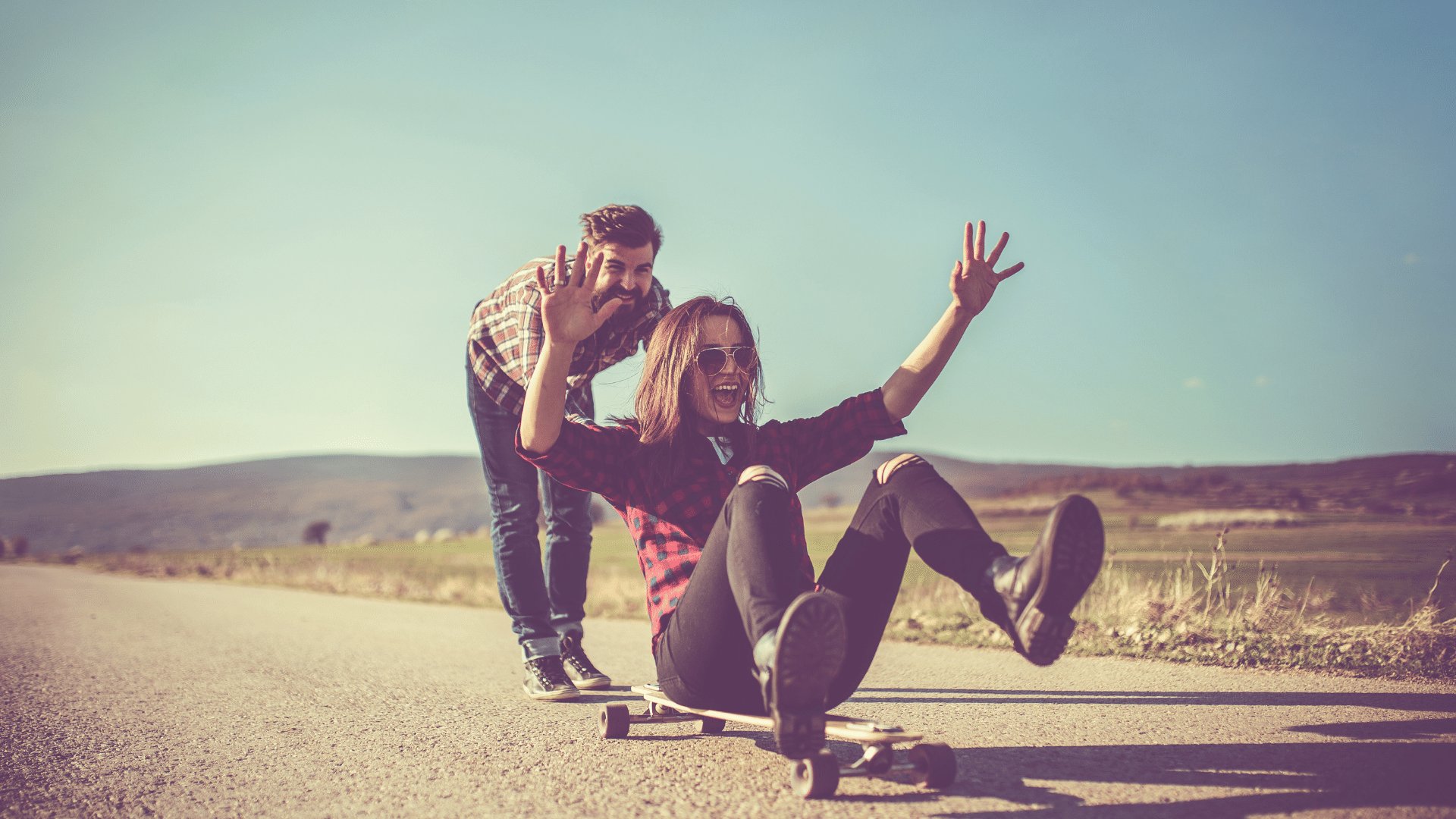 Mulher sentada em cima de um skate dando risada e se divertindo sendo empurrada por um homem