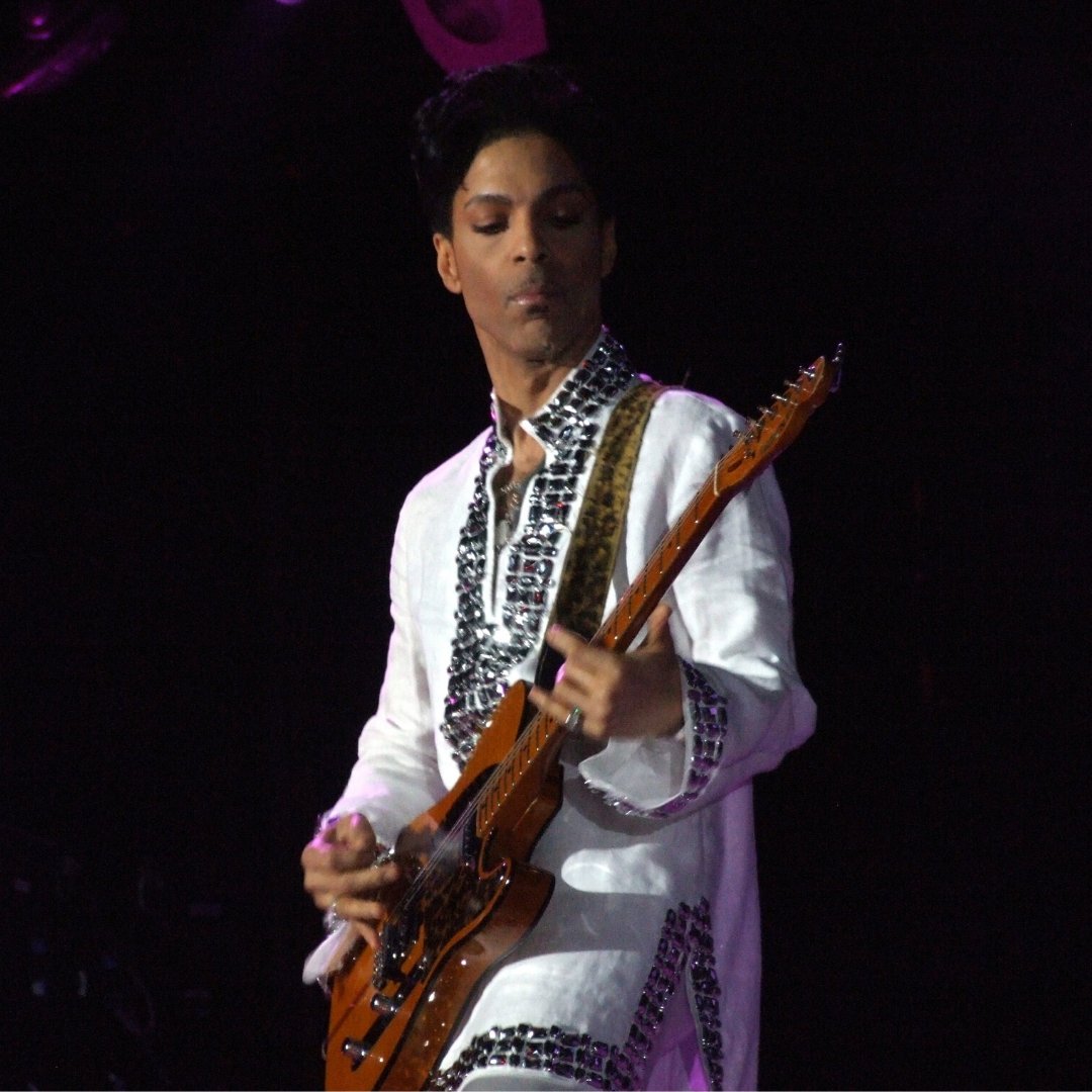 Cantor, músico e compositor Prince tocando guitarra durante show