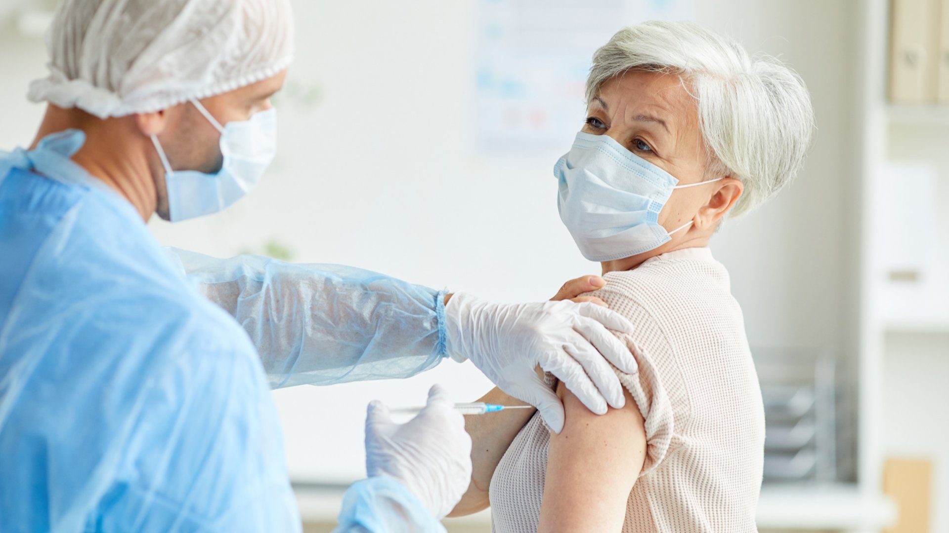 Mulher de máscara tendo a vacina aplicada em seu braço esquerdo por um homem também de máscara