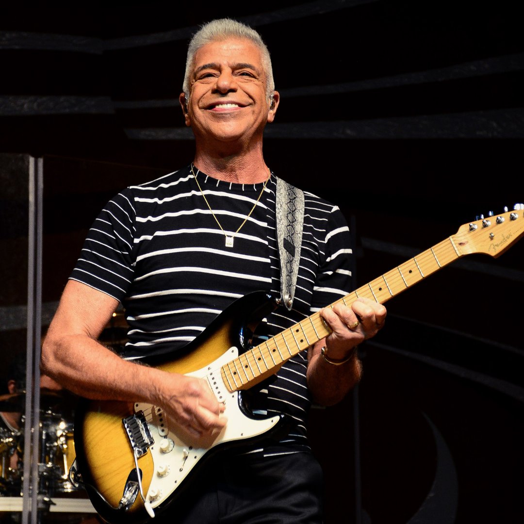 Imagem do cantor e compositor Lulu Santos tocando guitarra e sorrindo durante show