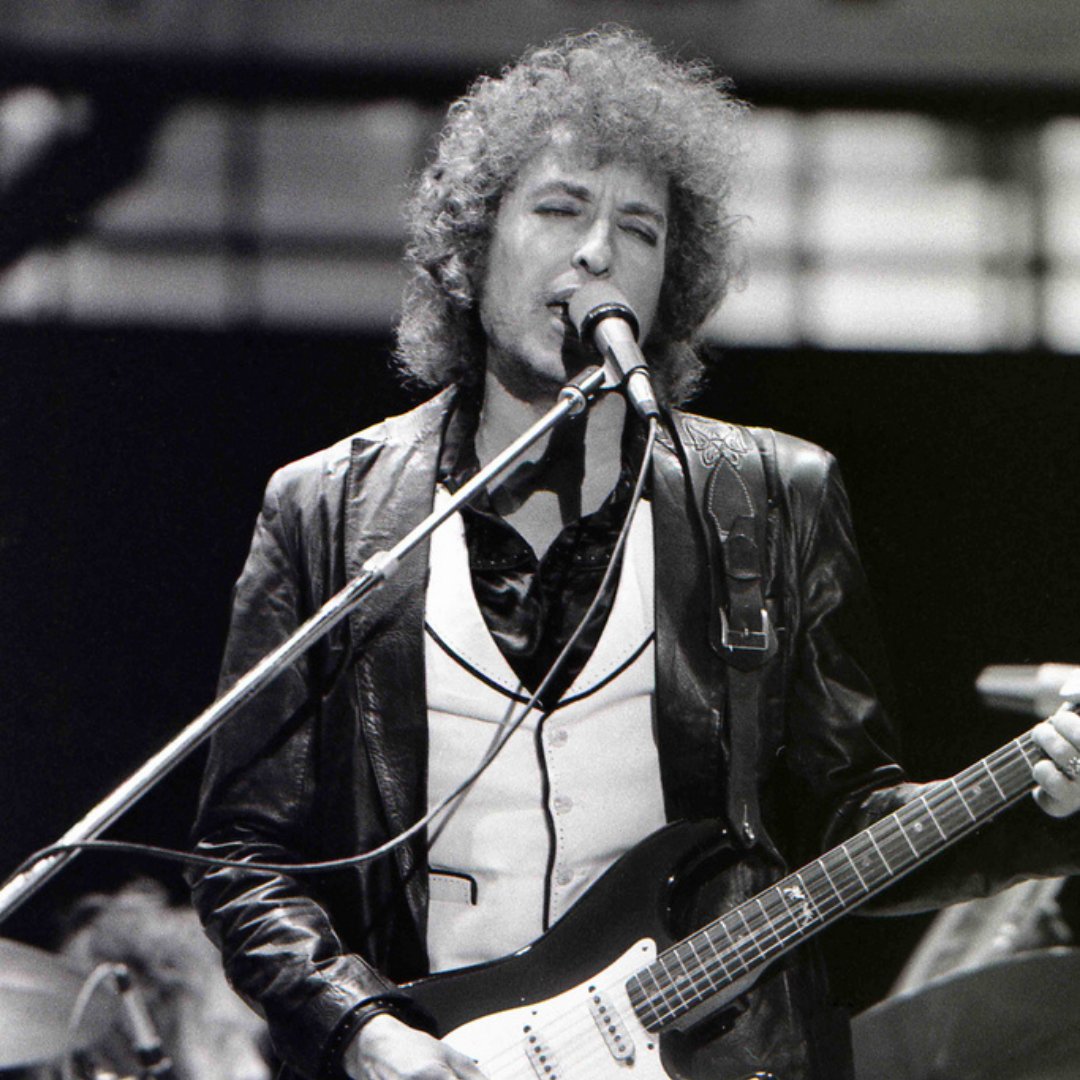 Imagem do cantor e compositor Bob Dylan cantando e tocando guitarra em um show