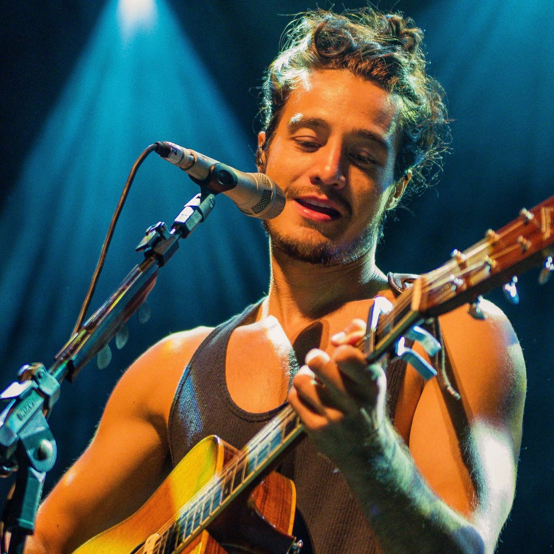 Imagem do cantor Tiago Iorc cantando e tocando violão em um show