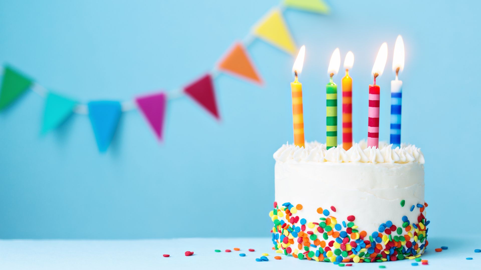 Ruth Black / Canva Bolo de aniversário com bandeiras coloridas ao fundo