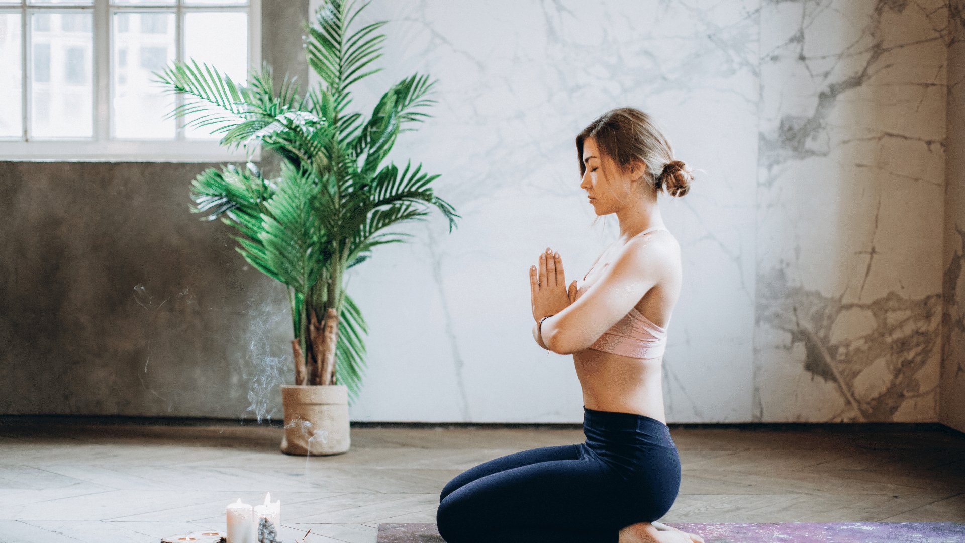 Mulher sentada em seu tapete em uma pose de yoga com as mãos unidas