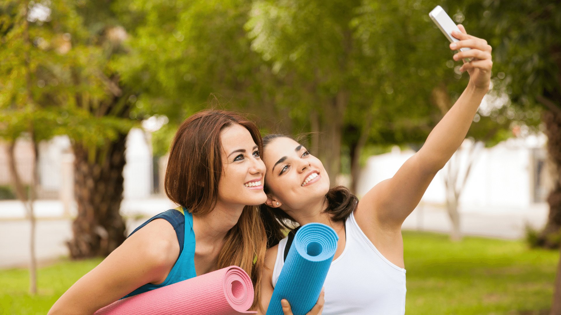 Duas mulheres segurando seus tapetes enrolados sorrindo ao tirarem uma selfie