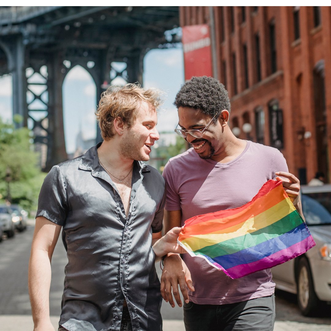 Dois homens sorrindo, um deles segurando a bandeira LGBT