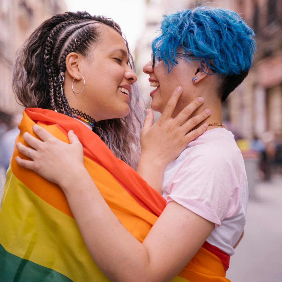 Casal sorrindo enroladas na bandeira LGBT
