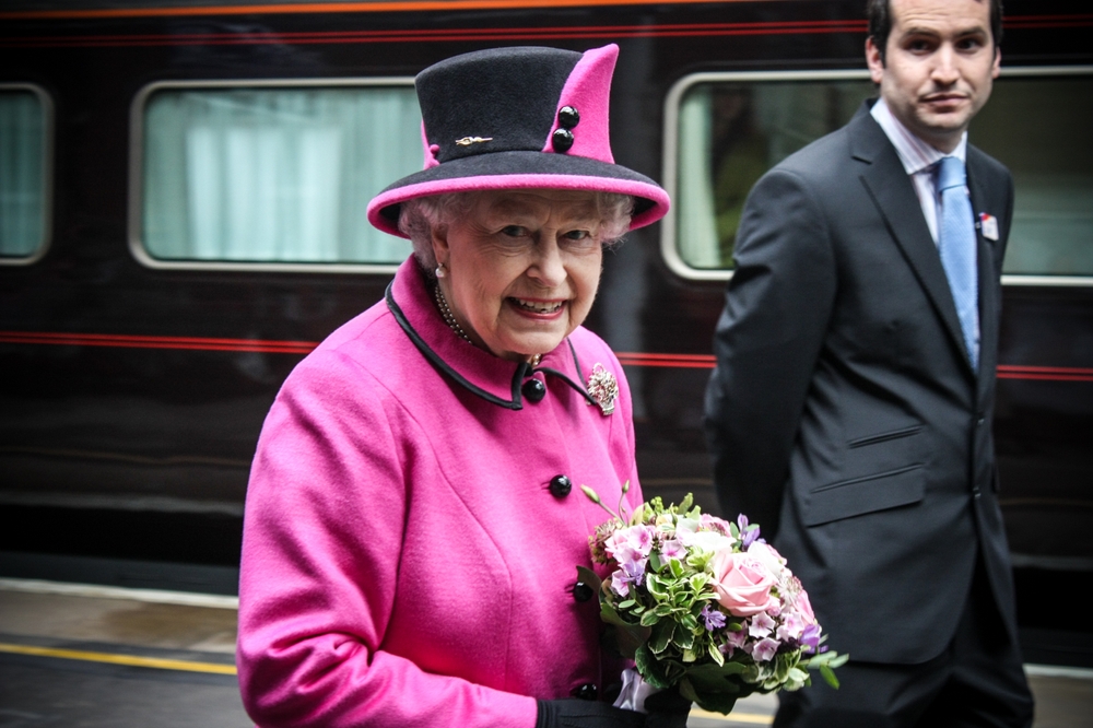 Rainha Elizabeth II de roupas rosas e segurando buquê de flores.