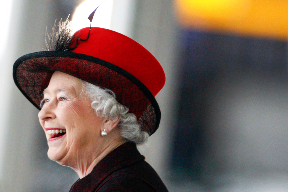 Rainha Elizabeth II sorrindo de chapéu vermelho.