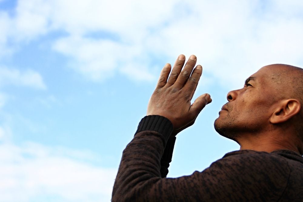 Homem com as mãos juntas em sinal de oração olhando para o céu