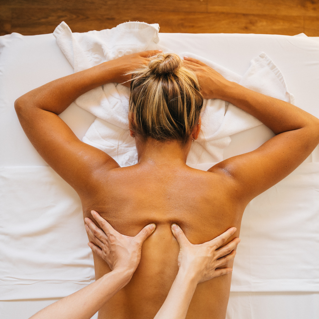 Mulher loira deitada de costas enquanto recebe massagem.