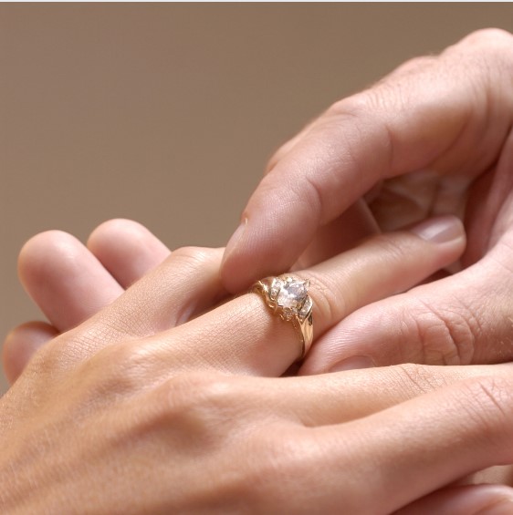 Homem colocando anel de noivado na mão de sua futura esposa.