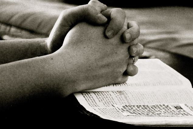 Mão fechada, representando oração, com uma Bíblia embaixo