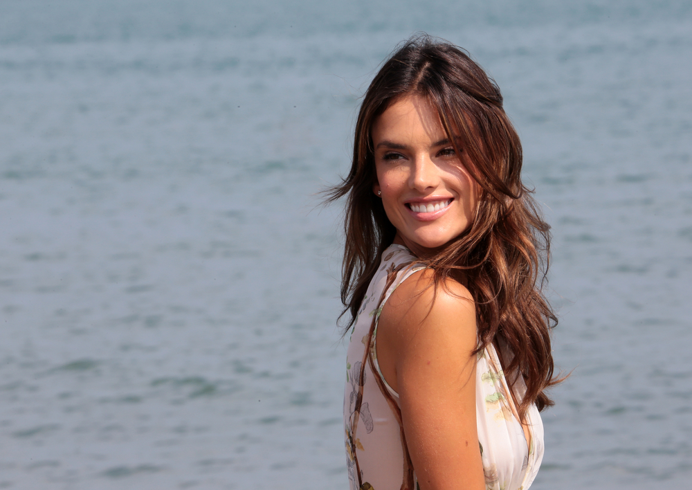 Alessandra Ambrosio parada em frente a um mar, sorrindo