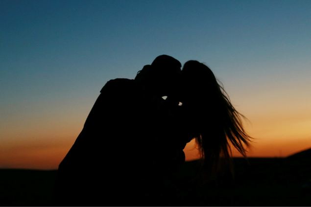 Silhueta da casal se abraçando com um pôr do sol na frente deles.