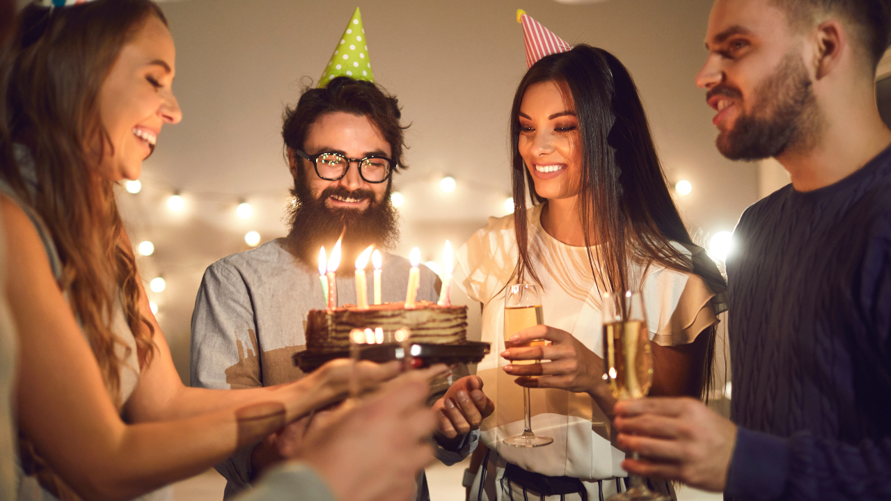 Adultos comemorando aniversário, segurando bolo e com chapéuzinhos de festa