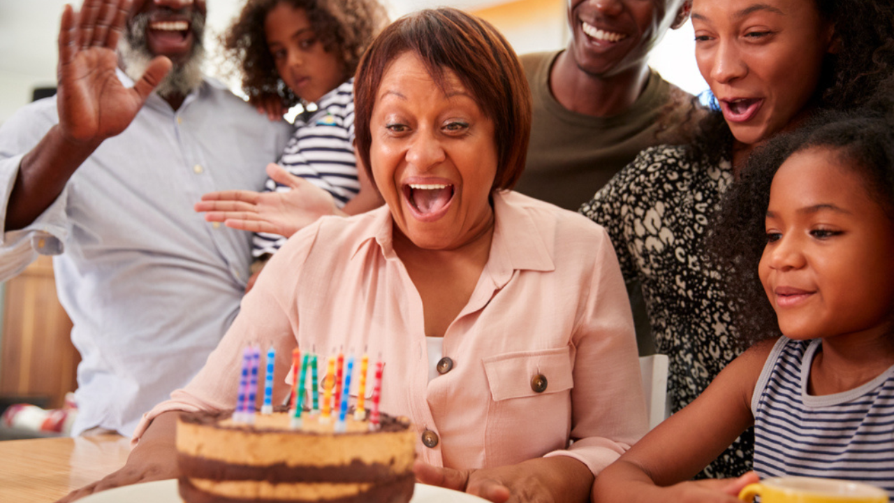 Mulher comemorando os 50 anos ao lado de sua família. Na frente dela, há um bolo