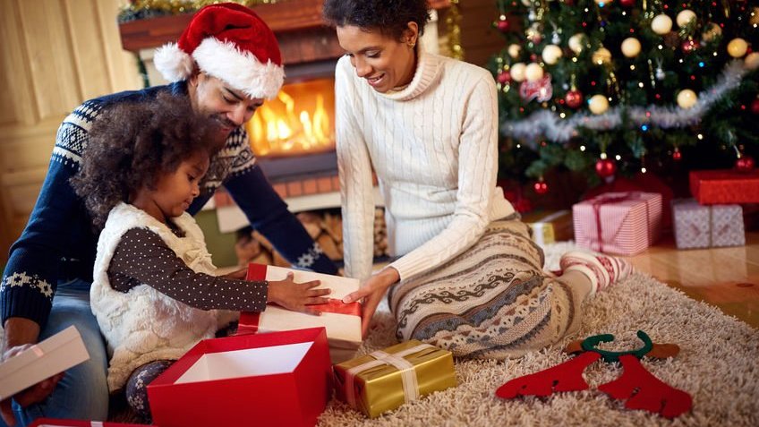Pais sorrindo abrindo presentes de natal com a filha