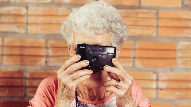 Mulher idosa com uma câmera analógica na mão cobrindo o rosto