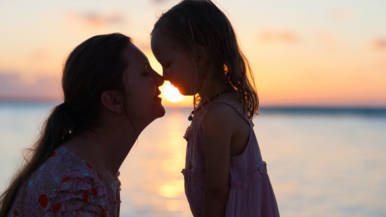 blueorange / Canva PRO Mulher e menina brancas com narizes encostados.