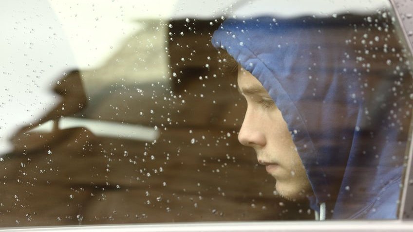 Menino adolescente triste dentro de um carro olhando pela janela.