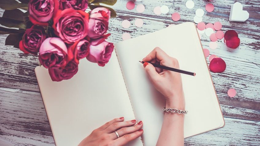 Mãos escrevendo carta vista de cima com vaso de rosas