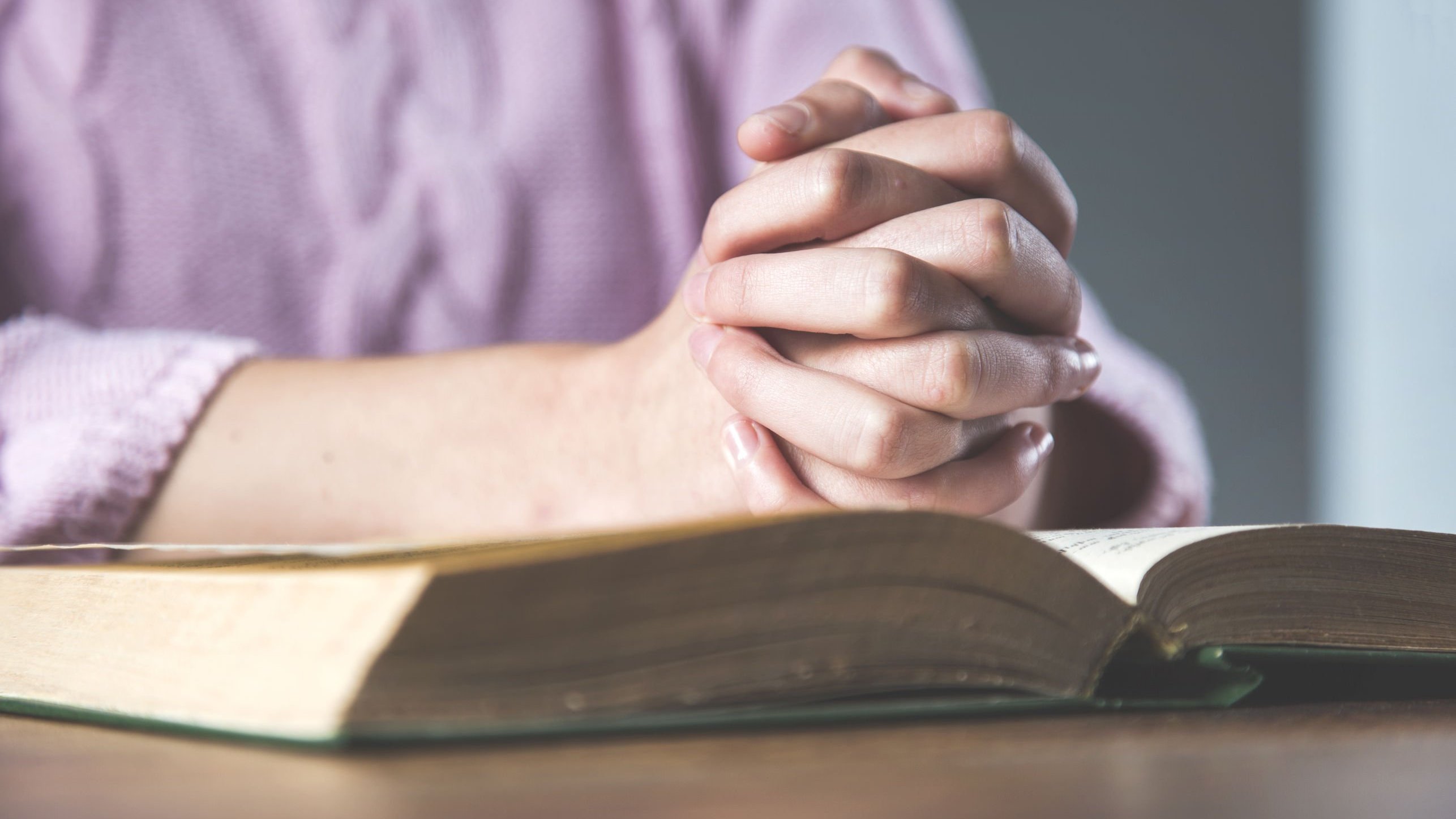 Pessoa com as mãos unidas em cima de uma bíblia aberta.