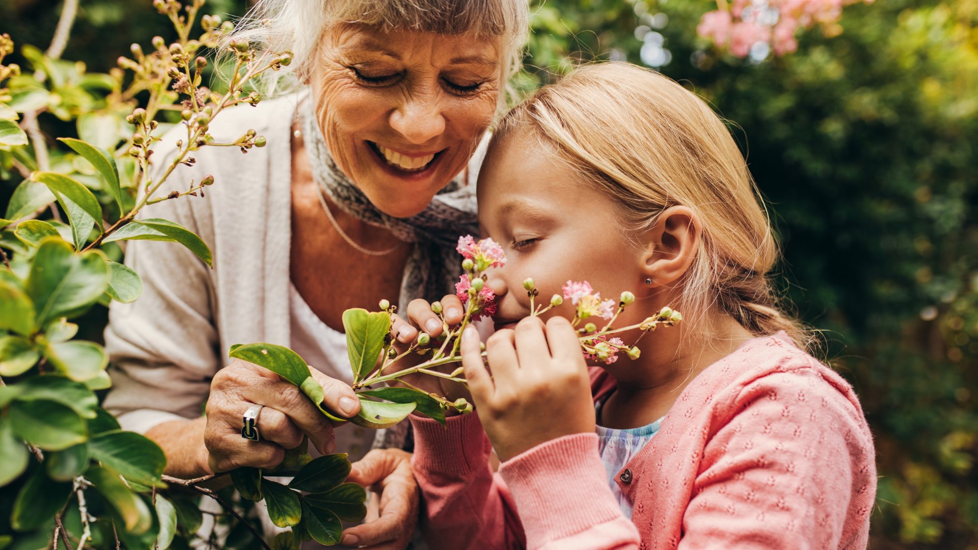 Avó e neta sorrindo no jardim enquanto cheiram flores