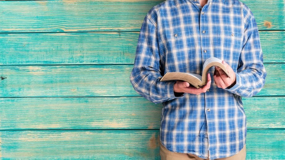 Pessoa em pé segurando bíblia com parede azul ao fundo