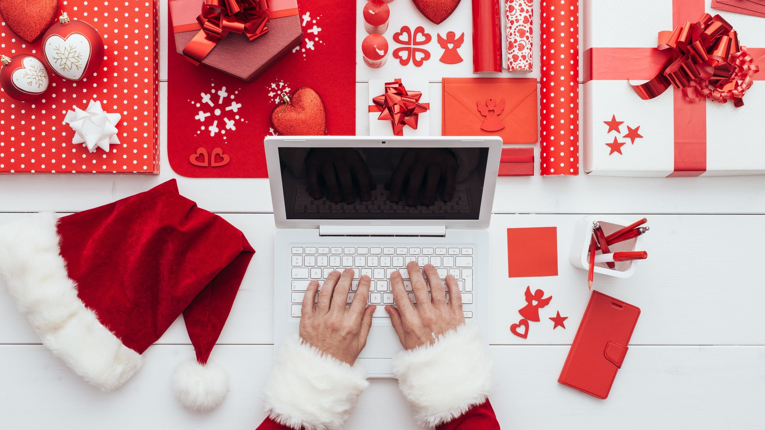 Mãos brancas manuseando um laptop branco com adereços natalinos ao redor.