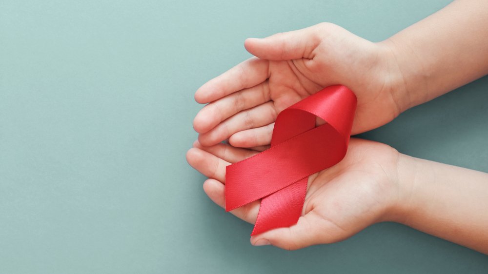 Mãos segurando fita vermelha como símbolo do Dezembro Vermelho.