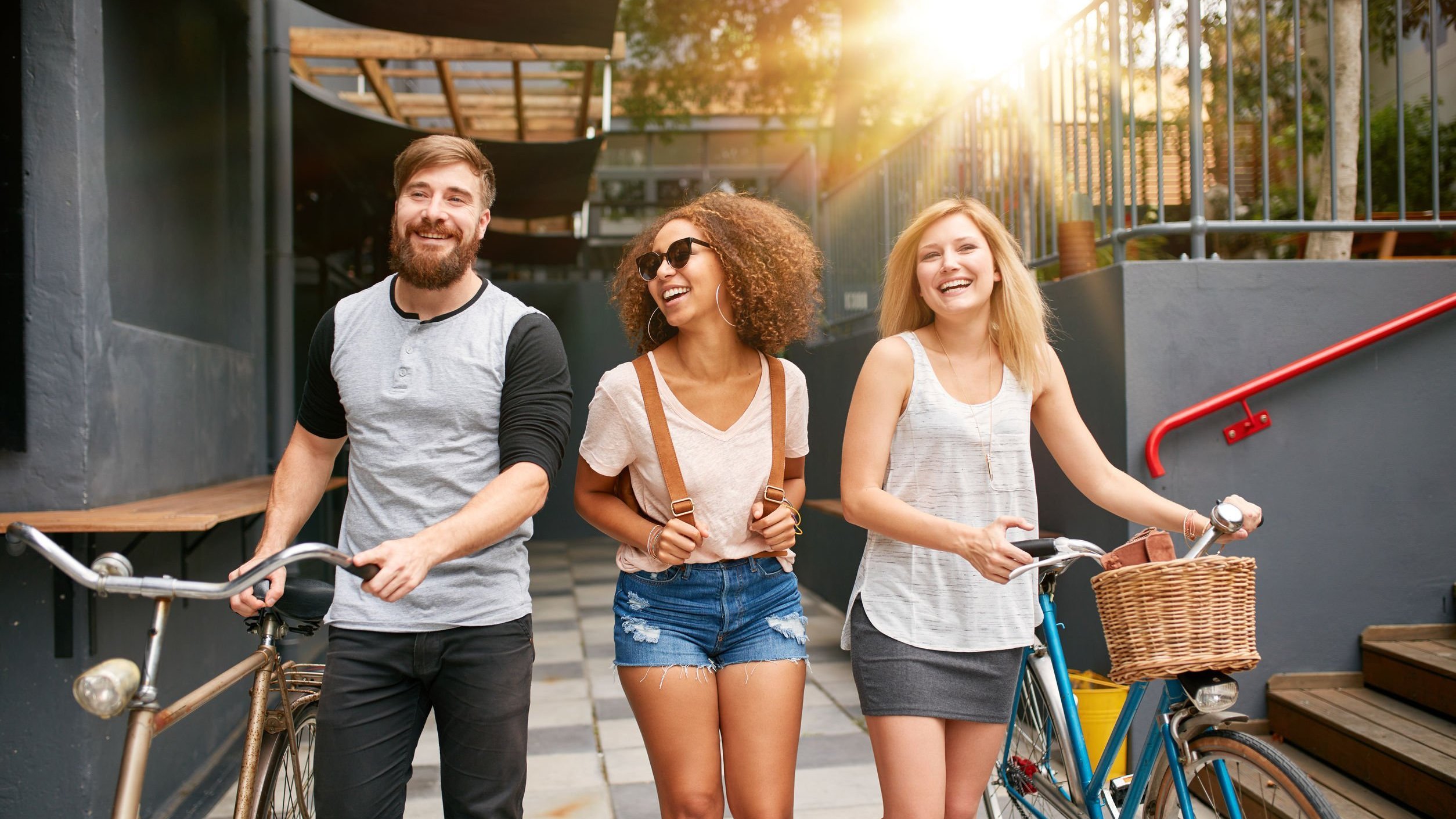 Três pessoas sorrindo e caminhando com bicicletas