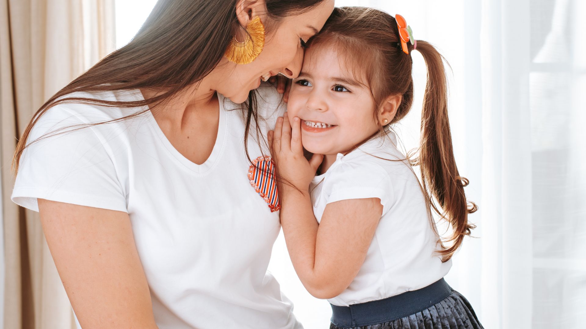 Imagem de mãe e filha abraçadas. Ambas vestem camiseta branca.