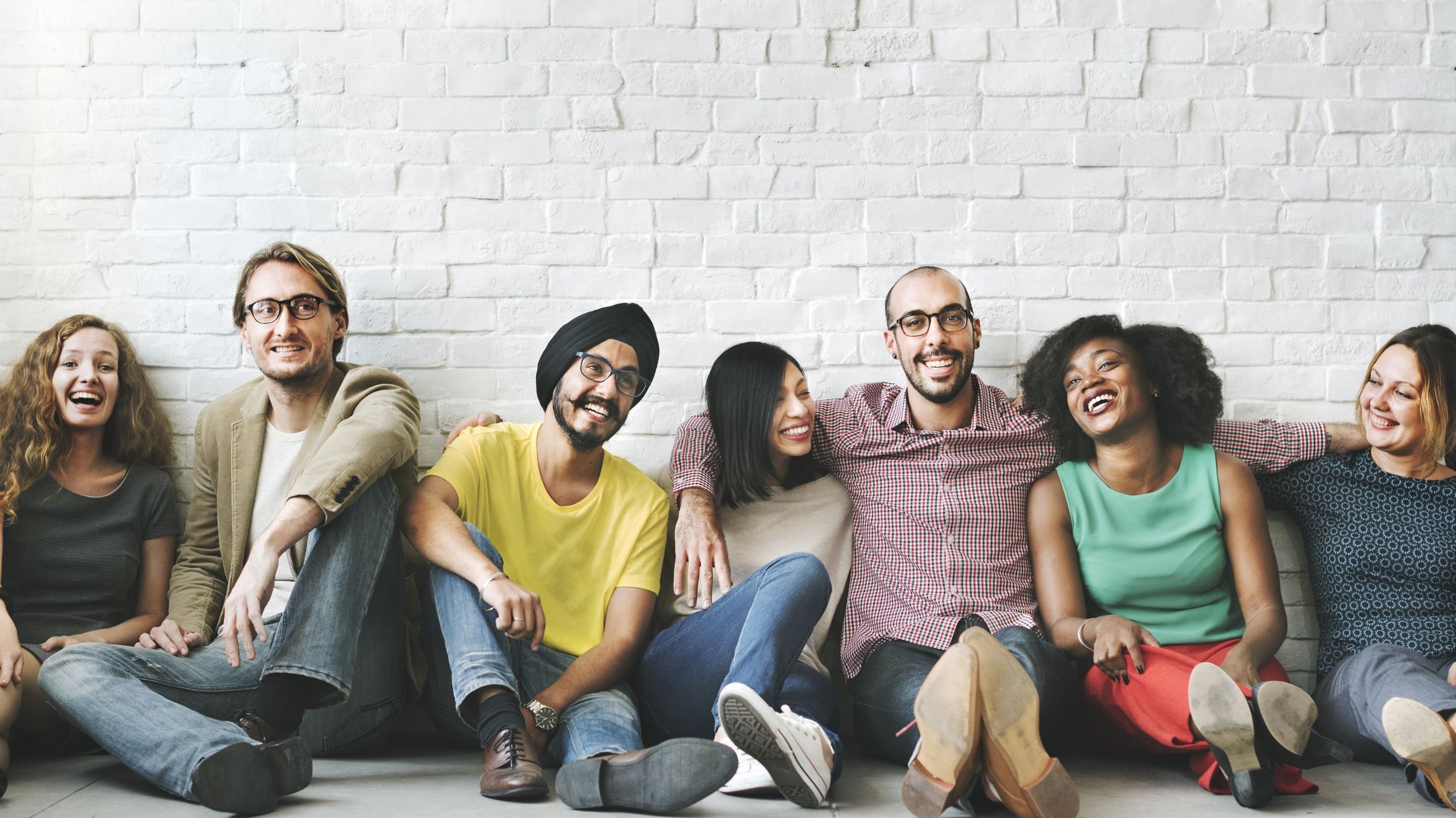 Grupo de amigos sentados no chão, lado a lado, sorrindo