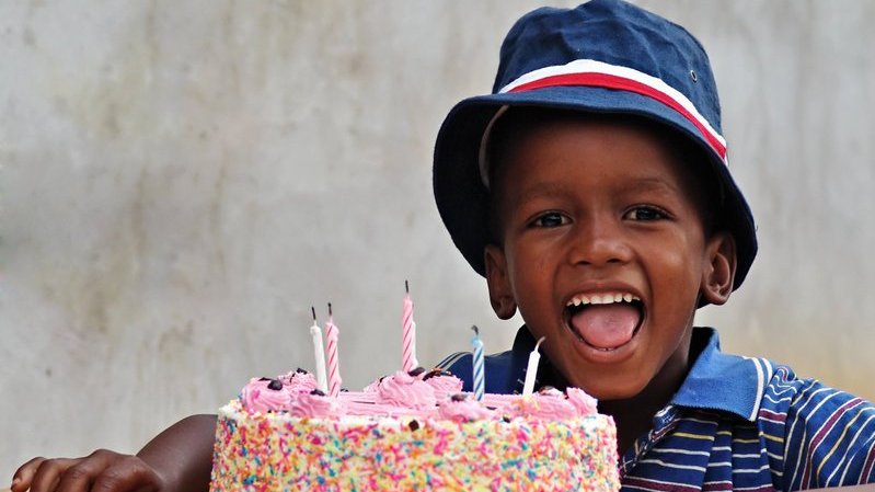 Menino negro sorrindo com bolo de aniversário.