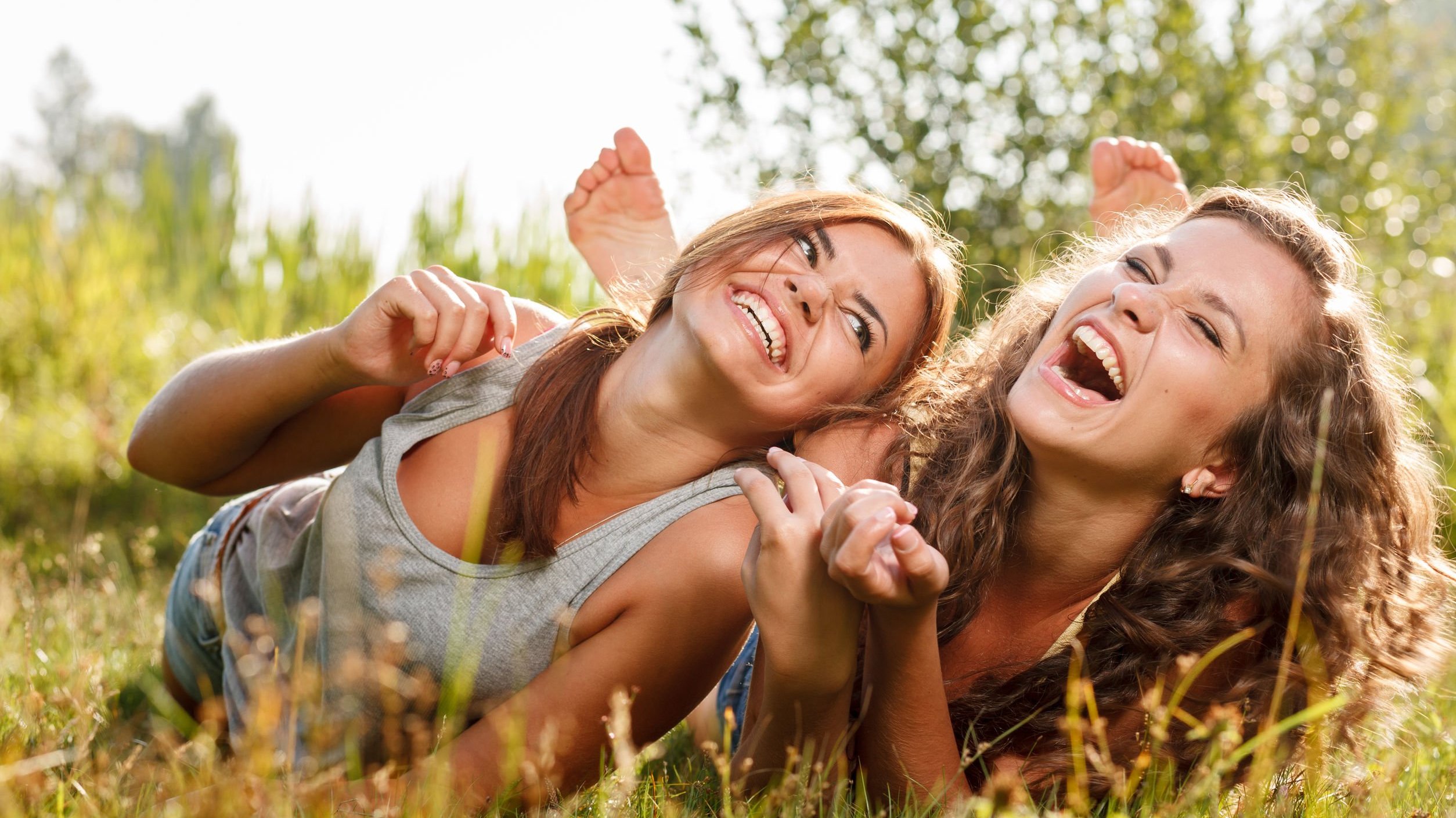 Duas amigas deitadas na grama, rindo.