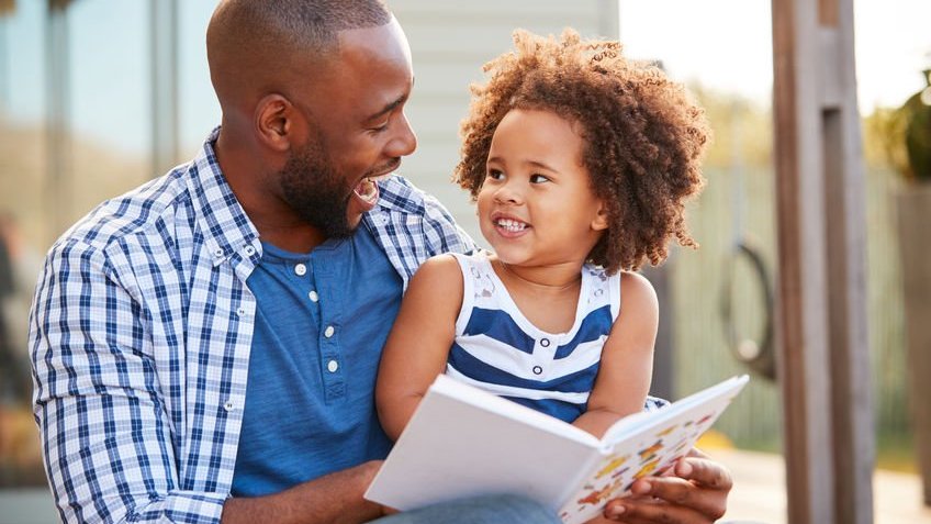 Pai com filho no colo e livro de histórias nas mãos sorrindo