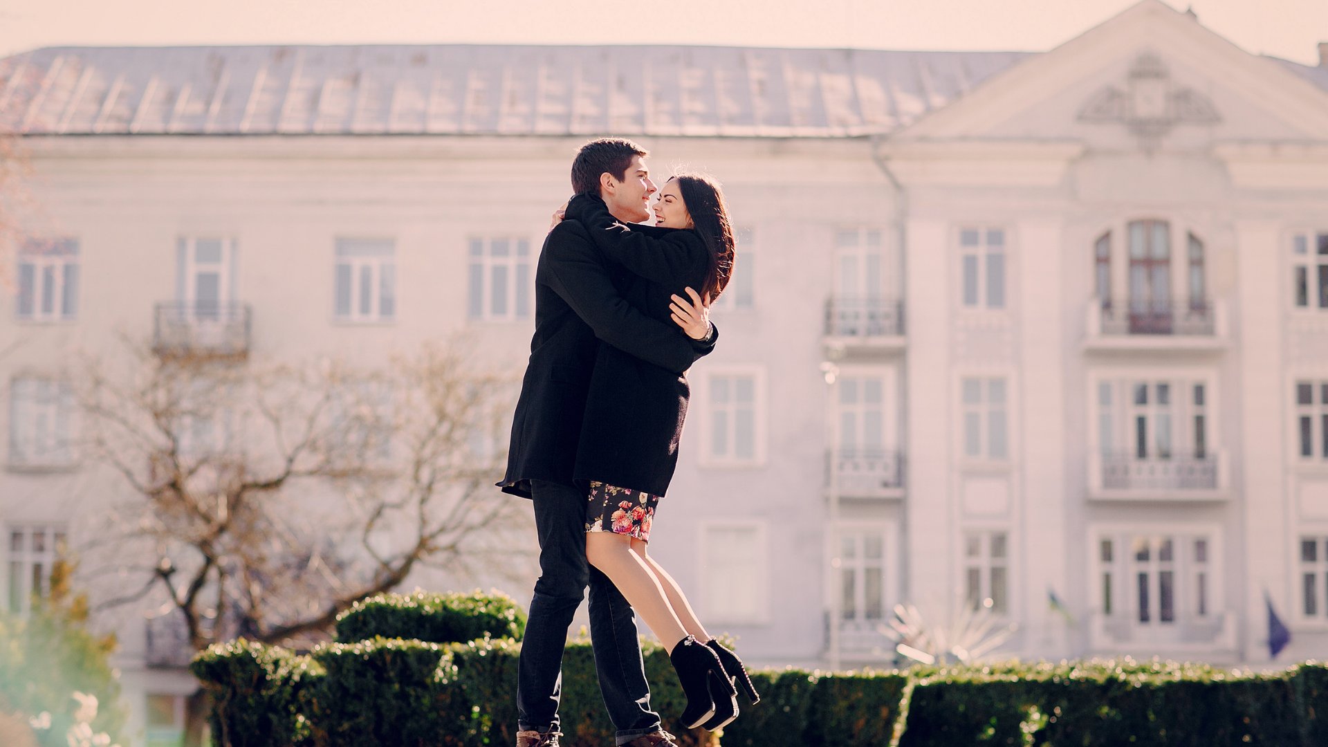 Casal abraçado em frente a uma mansão branca