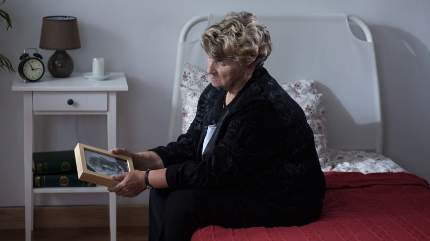 Senhora segurando foto de marido com expressão de saudade