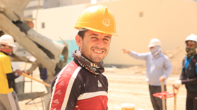 sumanamul15 / Pixabay Pedreiro jovem olhando para foto e sorrindo. No fundo, há vários ajudantes da obra