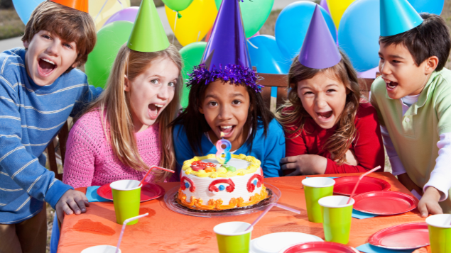 Crianças felizes em uma mesa de aniversário com bolo e com decorações atrás