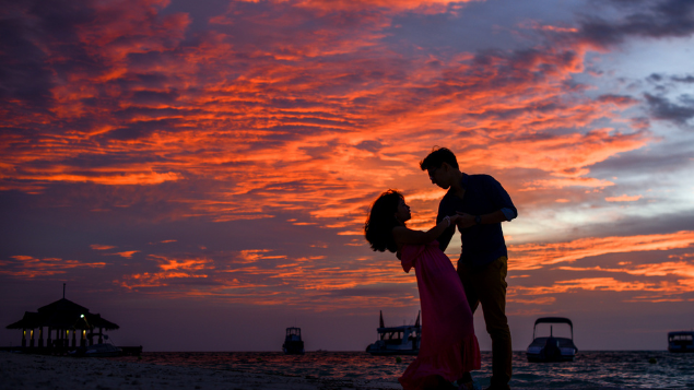 Asad Photo Maldives / Pexels Silhueta de casal dançando. Ao fundo, há um pôr do sol com algumas nuvens na frente